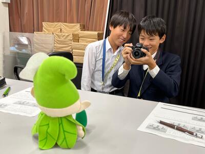 いこいーなの人形を撮影する生徒の画像