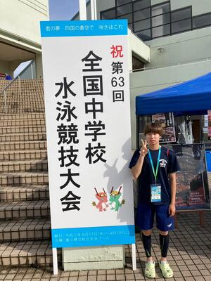 全国中学校水泳競技大会の看板の横に立つ森田選手