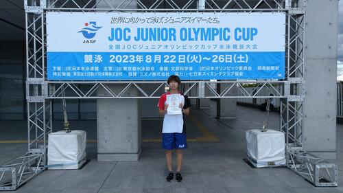 JOC ジュニアオリンピックカップ水泳競技大会の看板の前に立つ森田選手