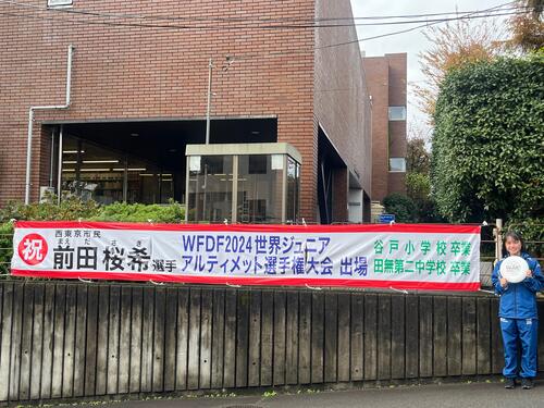 前田選手の活躍を広報した横断幕横に立つ前田選手の写真