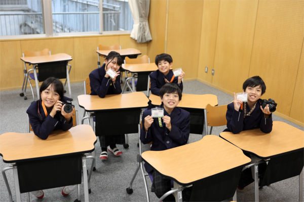 教室で名札やカメラを持って撮影した記念写真