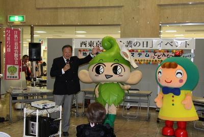 写真：「介護の日」イベント市長挨拶（「いこいーな」と西東京市社会福祉協議会マスコットキャラクター「福しんごうくん」）